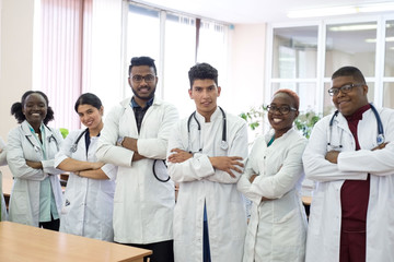 a group of doctors in the hospital corridor. Team of mixed race young men in white coats, with phonendoscopes, smiling