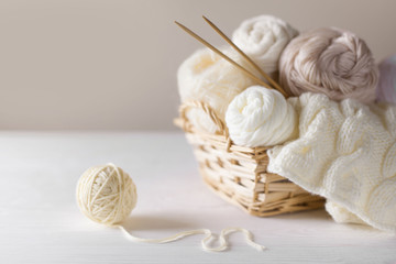 Fototapeta na wymiar White and beige yarn for knitting in a basket. Knitting needles.