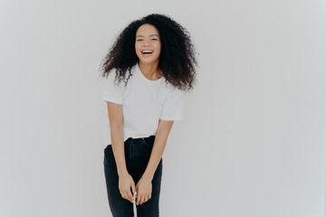 Studio shot of joyful African American woman laughs happily, dressed in casual wear, feels good, poses against white background with blank space for your advertising content, feels energized