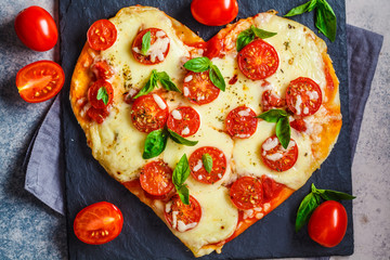 Heart pizza with mozzarella and tomatoes on slate, top view. Valentine's day date food concept.