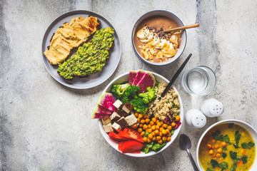 Flat lay of vegan food. Chocolate smoothie bowl, Buddha bowl with tofu, chickpeas and quinoa, lentil soup and toasts on a gray background.