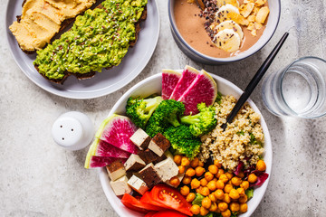 Flat lay of vegan food. Chocolate smoothie bowl, Buddha bowl with tofu, chickpeas and quinoa, toasts on a gray background.