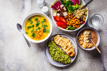 Flat lay of vegan food. Chocolate smoothie bowl, Buddha bowl with tofu, chickpeas and quinoa, lentil soup and toasts on a gray background.