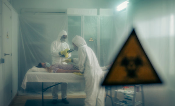 Two people attending to a woman with a virus lying on a stretcher in a field hospital with bio hazard symbol in the foreground
