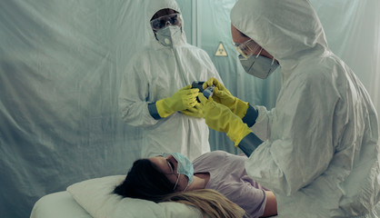Two people attending to a woman with a virus lying on a stretcher in a field hospital
