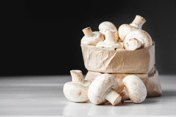 Mushrooms champignons in paper bag on a white wooden table on a dark background. Place for text or advertising