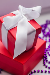Small red gift boxes tied with a white ribbon and purple Christmas beads on a light background. Cozy holiday home decorations