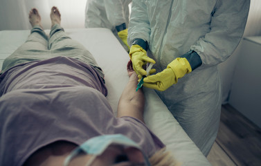Unrecognizable female doctor with bacteriological protective suit injecting antiviral to a sick...
