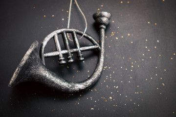 blurred vintage christmas toy in a shape of   metal musical trumpet on black background with gold sequins and copy space