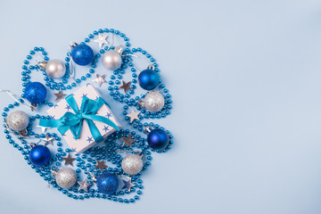 Christmas composition with gift box with a beautiful bow, beads, Christmas balls and stars on a blue background. Overhead flatlay with copy space for your text
