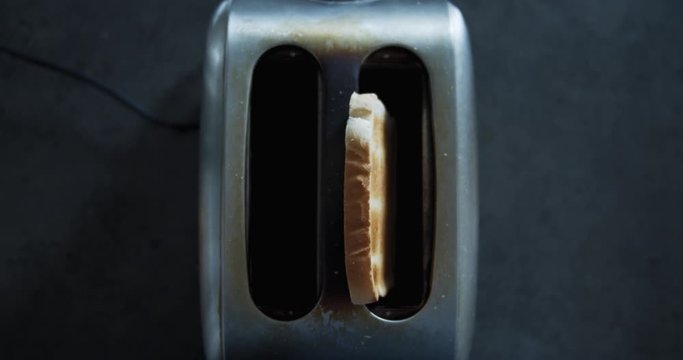 Zooming slow motion shot of a toaster from above shooting a roasted toast into the air