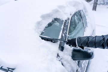 Hand are holding and brushing car window clean of snow. car covered in snow during heavy snow fall. Winter and seasonal concept.