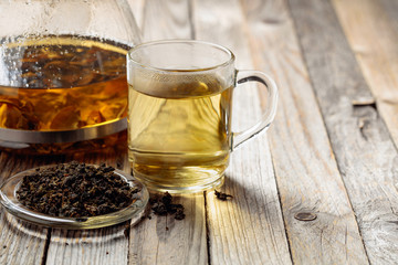 Hot green tea in glass mug. Dried tea leaves and hot drink on a wooden table.