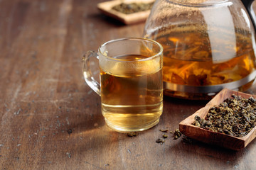 Hot green tea in glass mug. Dried tea leaves and hot drink on a wooden table.