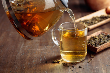 Fresh green tea is poured from a teapot into a mug.