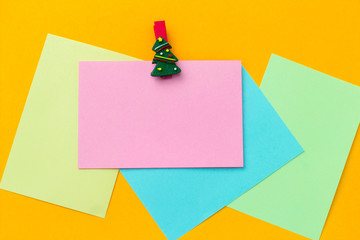 top view festive christmas clothespin and empty paper sheets with free space for text  on a vibrant yellow background