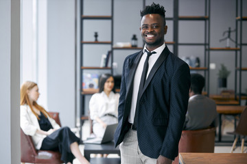 Personable businessman wearing formal black tuxedo stand posing in office environment and look at camera and smile . Business people concept