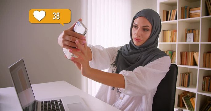 Closeup portrait of muslim female in hijab getting likes in social media using phone in office indoors