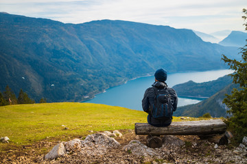 a man sits on a wooden bench on a hill and looks at an alpine landscape with a lake