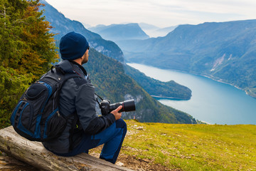 A man with a camera sits on a bench the background of a beautiful alpine landscape