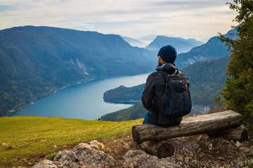 a man sits on a wooden bench on a hill and looks at an alpine landscape with a lake