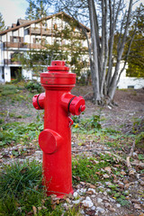 Fototapeta na wymiar Red fire hydrant in focus. Wooden house is blurred