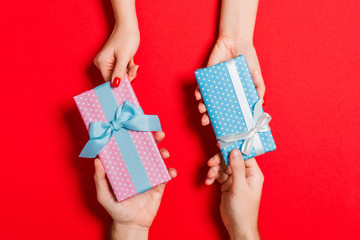 Top view of a woman and a man exchanging gifts on colorful background. Couple give presents to each other. Close up of making surprise for holiday concept - obrazy, fototapety, plakaty