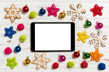 Top view of tablet on holiday wooden background. New Year decorations and toys. Christmas concept