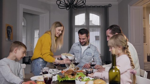 Smiling charming woman putting spaghetti on plates for her all relatives during family dinner