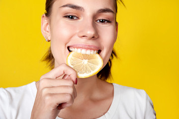 Girl bites a slice of lemon. Close-up, on a bright yellow background. Healthy nutrition, cold prevention, vitamins.