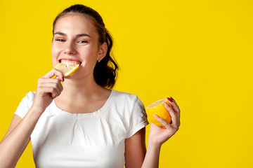 A girl in a white T-shirt is eating a lemon, on a bright yellow background. Free space for text.
