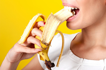 Girl bites a banana, very close-up, on a bright yellow background.