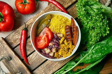 Vegetarian bowl with couscous, soy sausage, cucumbers and salad on a wooden tray in a composition with fresh vegetables. Healthy and balanced food.