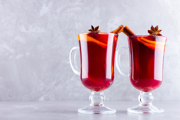 Two glasses of mulled wine with spices on cement background. Christmas mulled wine with orange, star anise and cinnamon. Red mulled wine on a gray background. Minimalism. Copy space