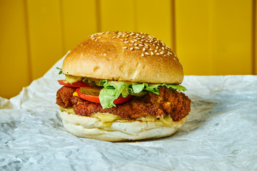 Juicy burger with melted cheese with a meat patty on craft paper. Yellow background. Street, fast food. Close up. Copy space.