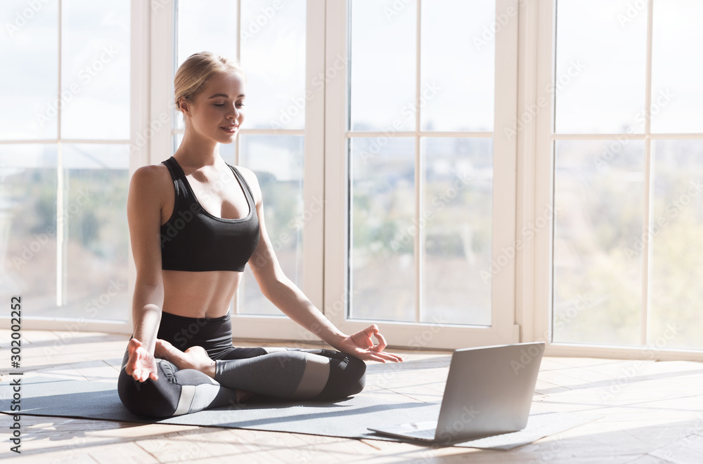 Wall mural cheerful girl doing yoga at home, looking at laptop screen