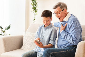 Grandson Teaching Grandpa Use Phone Sitting On Sofa At Home
