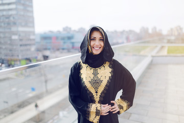 Gorgeous muslim woman in traditional wear looking at camera and posing while standing on rooftop.
