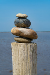 A stack of colorful stones on a wooden column in front of the sea and the blue sky