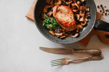 Chicken with mushrooms in a pan lies on a light background Chicken lunch next to vintage cutlery
