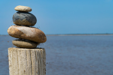 A stack of colorful stones on a wooden column in front of the sea and the blue sky