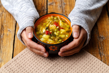 Female hands hold a plate with vegetable soup with chicken. Plate with soup and croutons on a wooden background. Healthy eating concept.