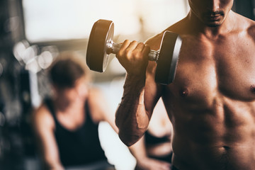 Muscular bodybuilder guy doing exercises with dumbbells in gym