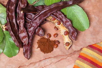 Carob. Organic carob pods with seeds and leaves on tree bark table. Healthy eating, food background.