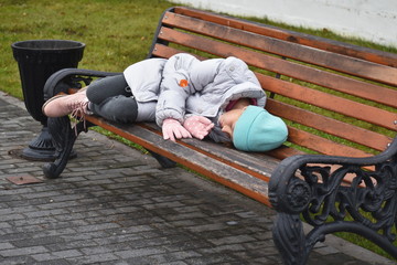 Homeless girl sleeping on bench autdoor. Girl teenager lies on bench in autumn.