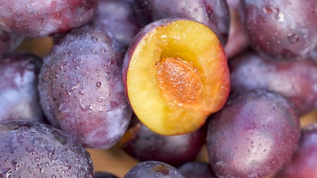 Close-up of fresh juicy wet plums on a wooden table, on top half a plum with a stone. Fruit covered with droplets of water. 360 rotation.