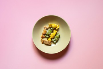 Stuffed Pasta with caramelle shape served in a cream bowl over a coral pink background top view