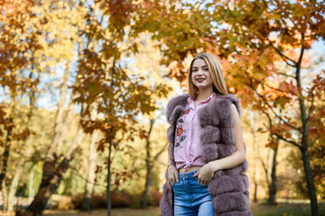 Fototapeta na wymiar Fashion woman. Smiling girl in fur coat posin in autumn park with trees and ivy