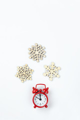 Simple Christmas composition. Small analog red clock, wooden snowflakes on white background. Minimal style flat lay, for social media. Top view. Celebration concept