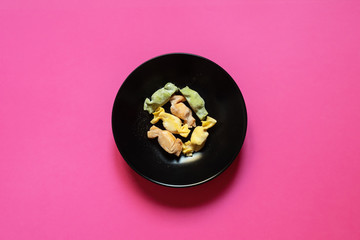 Stuffed Pasta with caramelle shape served in a black bowl over a pink background